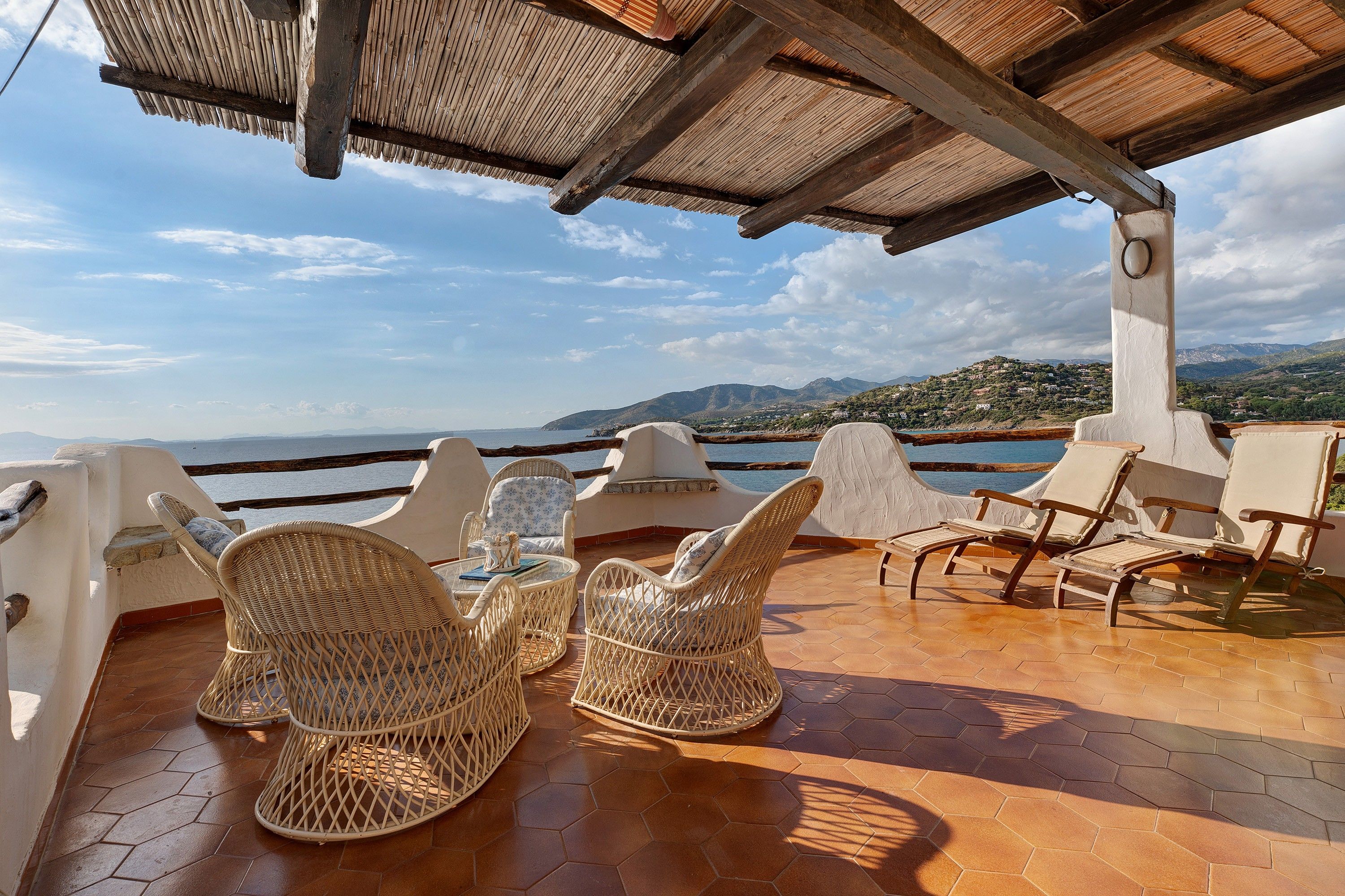 Una terrazza con mobili in vimini e vista sul mare e sulle montagne.