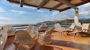 Una terrazza con mobili in vimini e vista sul mare e sulle montagne.