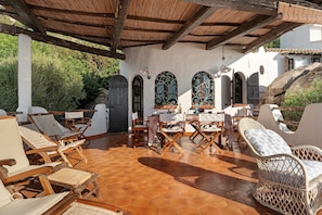 A covered outdoor seating area with hexagonal tiled flooring, wooden furniture, and a pergola structure.