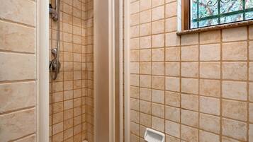 Un bagno con pareti piastrellate color crema, una doccia con porta in vetro e una piccola finestra con inferriate decorative.