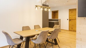 Un comedor moderno con una mesa y sillas de madera, una lámpara colgante y una cocina al fondo.