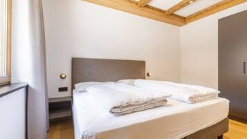 A bedroom with a bed, wooden ceiling beams, a window with curtains, and a wardrobe.