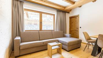A modern living room with a sectional sofa, a small wooden table, and a dining area with chairs.