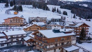Un centro de esquí cubierto de nieve con varias construcciones de estilo chalet, un telesilla y montañas al fondo.