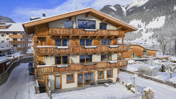 Un hotel de varios pisos con balcones, una pista de esquí al fondo y un paisaje nevado.