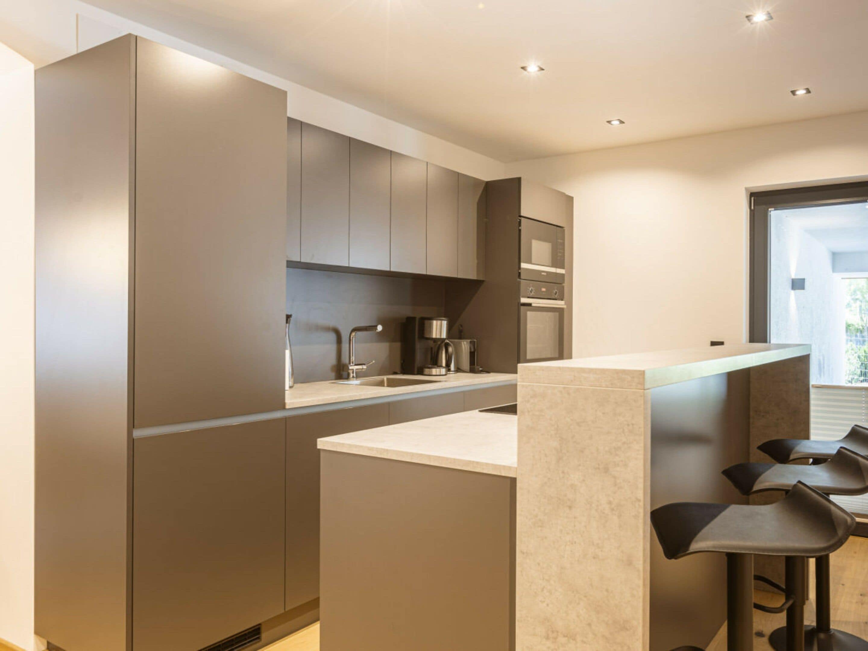 A modern kitchen with a central island, bar stools, and built-in appliances.