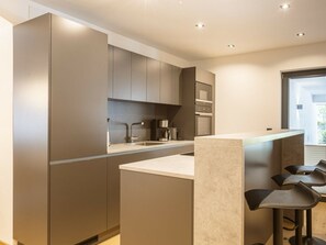 A modern kitchen with a central island, bar stools, and built-in appliances. - Apartment in Lermoos With Terrace (Lermoos)