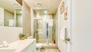 Een moderne badkamer met een douchecabine van glas, een witte wastafel en een toilet.