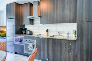 Ett modernt kök med mörka träskåp, rostfria vitvaror och en kakelbeklädd vägg bakom arbetsbänken.