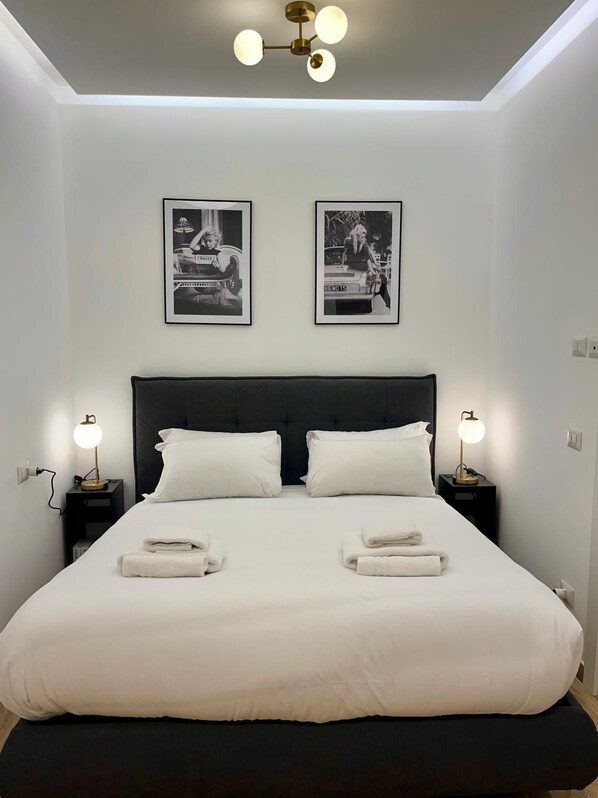 Ein modernes Schlafzimmer mit einem großen Bett, zwei Nachttischen mit Lampen und zwei gerahmten Bildern an der Wand.