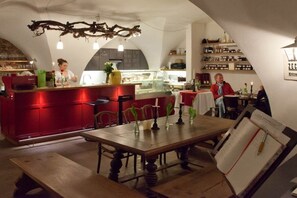 A restaurant with a red counter, wooden tables, and a hanging branch light fixture. - 4 Weingut Hauerhof 99 (Klosterneuburg)