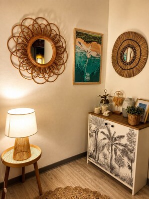 A room with a round mirror, a framed painting, a cabinet with botanical prints, a lamp, and a woven rug. - Villa Saint-Jo – Sleeps 15, ocean view, heated pool in winter (Saint-Joseph)