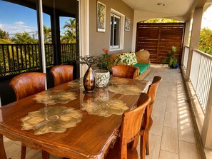 A wooden dining table with chairs, a vase, and a potted plant on a balcony with a view of palm trees.