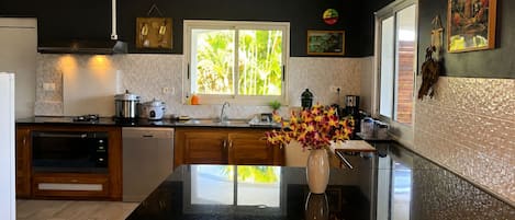 A modern kitchen with a black countertop, wooden cabinets, a window with a view of greenery, and a vase with flowers on the island.