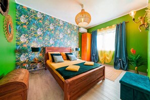 A room with a bed, a wooden headboard, a wall with a floral pattern, a hanging light fixture, and a window with curtains. - Villa Saint-Jo – Sleeps 15, ocean view, heated pool in winter (Saint-Joseph)