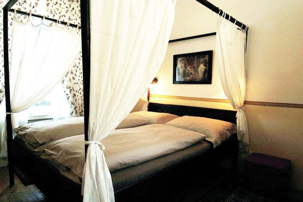 A four-poster bed with white curtains, a bedside table, and a wall-mounted picture.