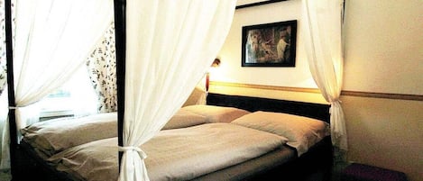 A four-poster bed with white curtains, a bedside table, and a wall-mounted picture.
