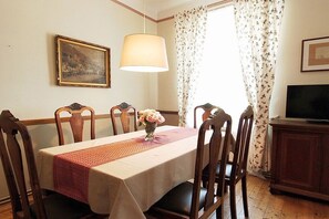 A dining area with a table set for four, a vase of flowers, a painting on the wall, and a television on a cabinet. - 2 Weingut Hauerhof 99 (Klosterneuburg)