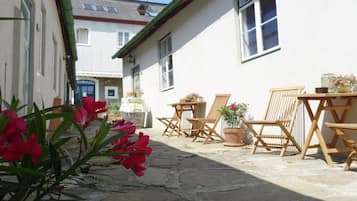 A courtyard with stone flooring, wooden furniture, and potted plants.
