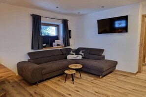 Un salon moderne avec un canapé d’angle, une petite table en bois et un téléviseur à écran plat fixé au mur.