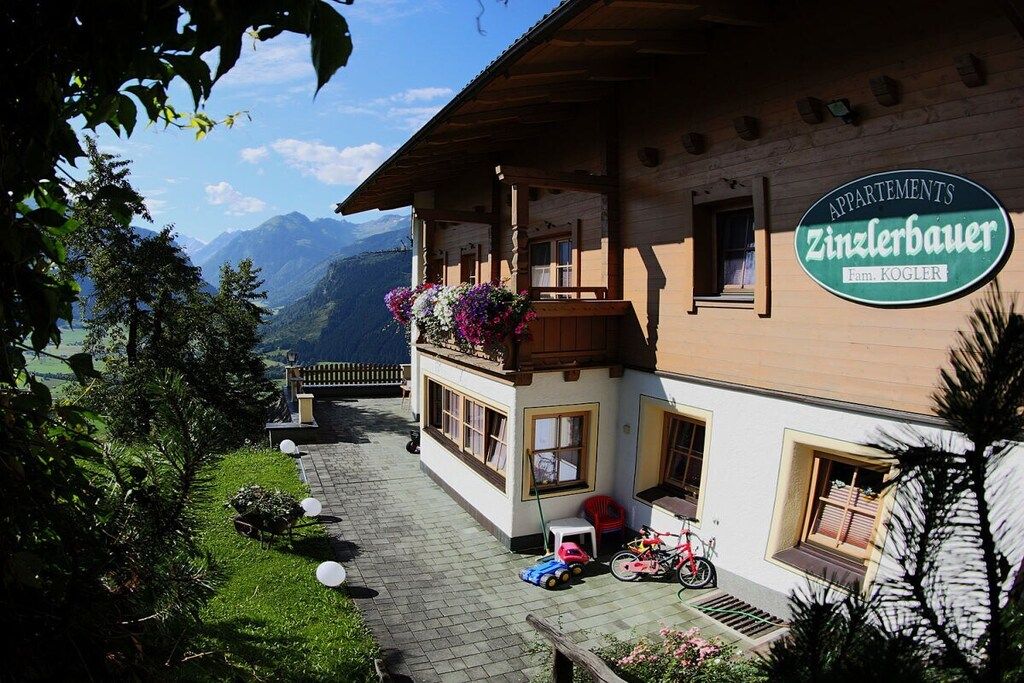 Un bâtiment en bois doté d’un balcon, une enseigne indiquant « APPARTEMENTS Zintlberauer », et une vue sur les montagnes en arrière-plan.