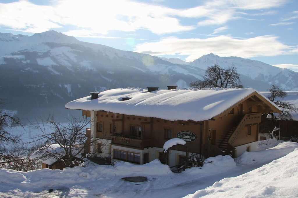 A chalet with a snow-covered roof, a staircase, and a sign indicating it is a Zinslerbauer property.