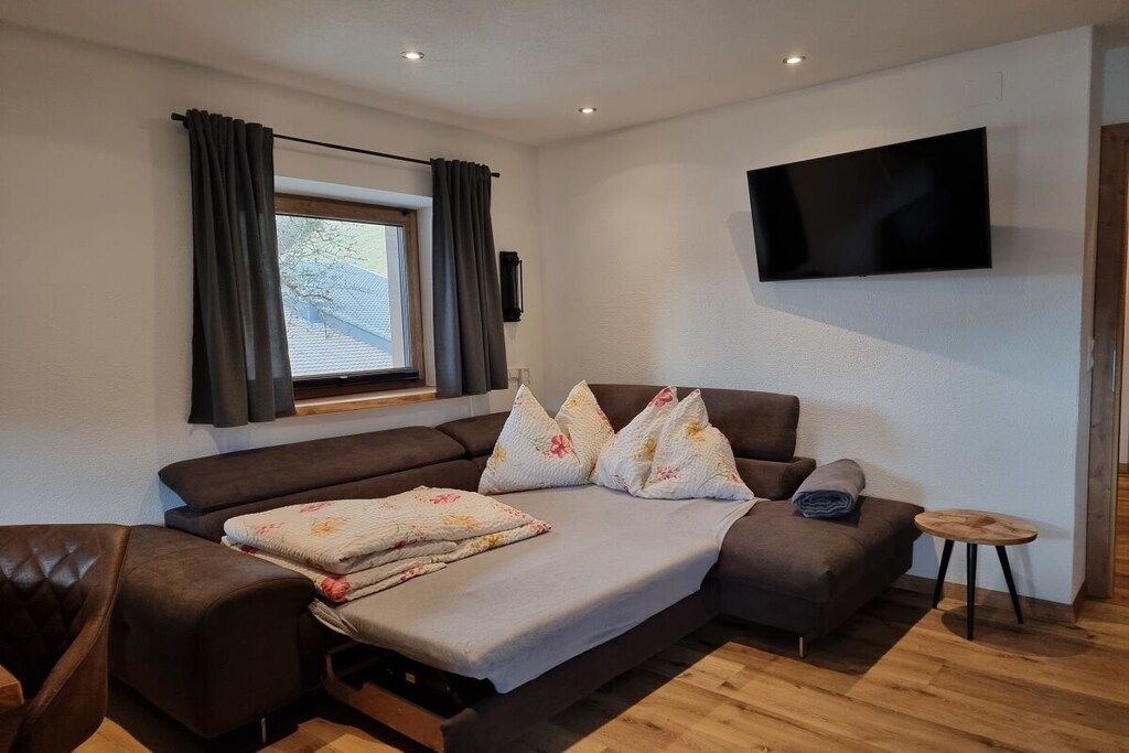 A modern living room with a sofa, a television mounted on the wall, and a window with curtains.