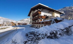 A multi-story building with balconies, surrounded by snow-covered ground and mountains in the background. - Alpenstern Apartment Ahorn (Ramsau)
