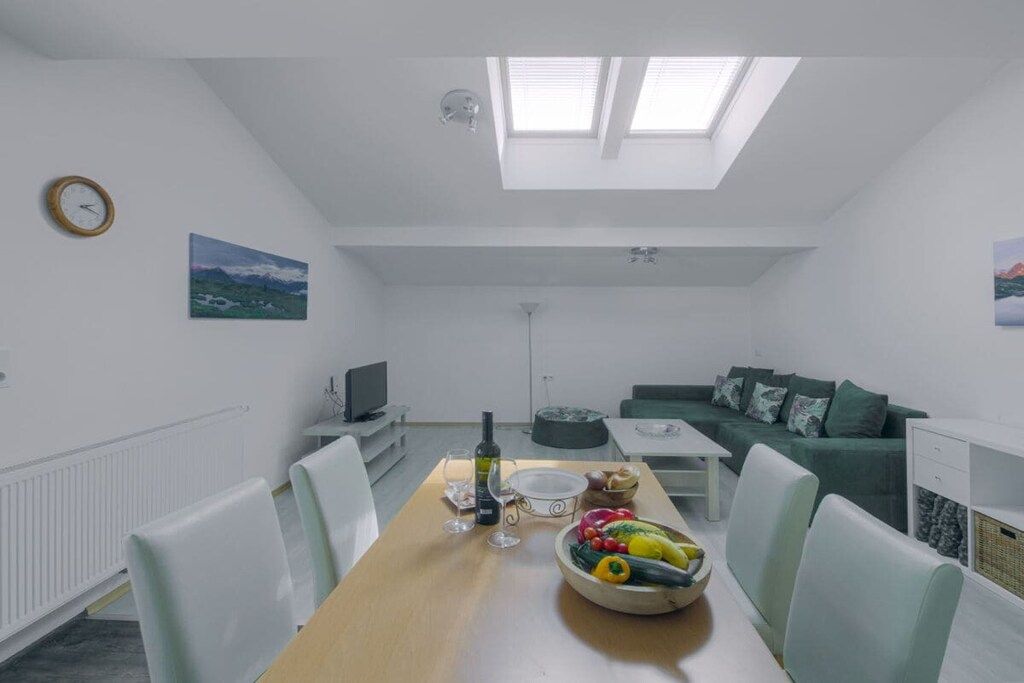 Una sala de estar moderna con comedor, que incluye una mesa de madera, un tazón de frutas, una botella de vino y un sofá verde.