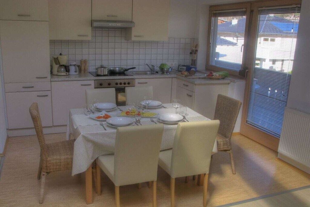 Cocina compacta con armarios blancos, estufa y mesa de comedor preparada para cuatro personas.
