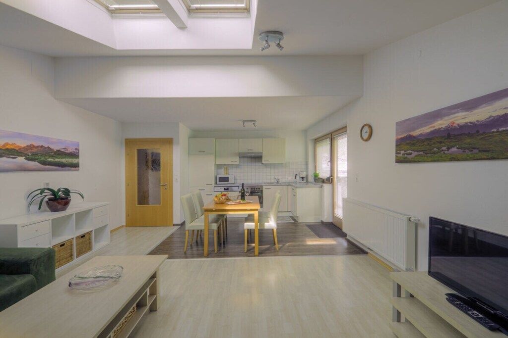 A modern living room with a dining area, a kitchen in the background, and a TV on the right.
