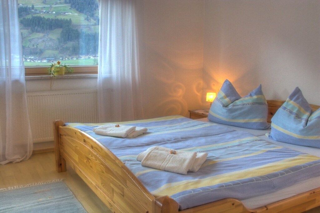 A room with a wooden bed, a window with a view of a landscape, and a bedside table with a lamp.
