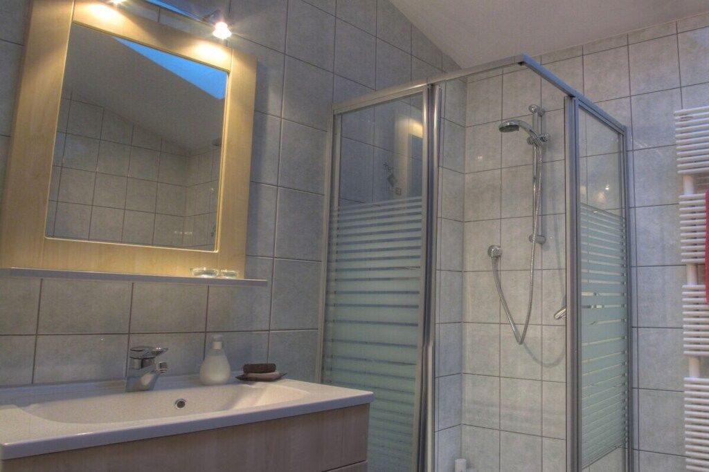 Casa de banho com chuveiro separado por vidro, lavatório com espelho e porta-toalhas.