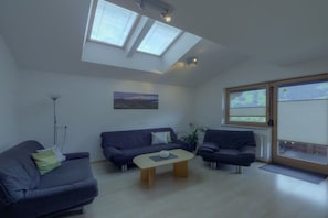 A modern living room with a sofa, armchair, and coffee table. There are skylights and a large window. - Alpenstern Fewo Tristner (Ramsau)
