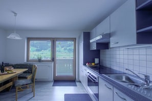 A modern kitchen with a dining area, a window with blinds, and a view of the outdoors. - Alpenstern Fewo Tristner (Ramsau)