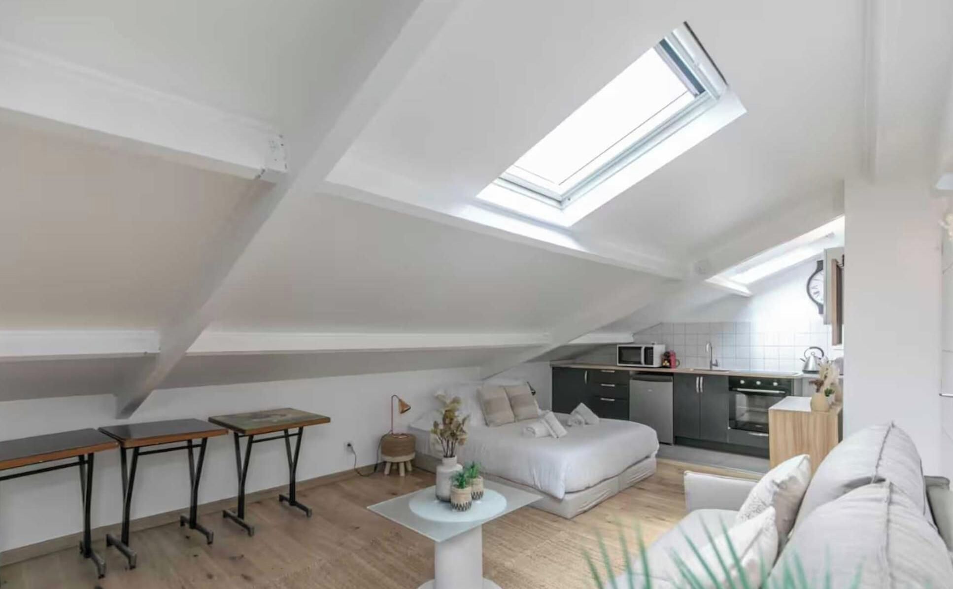 En lägenhet i loftstil med ett takfönster, ett litet kök, en säng och en liten matplats.