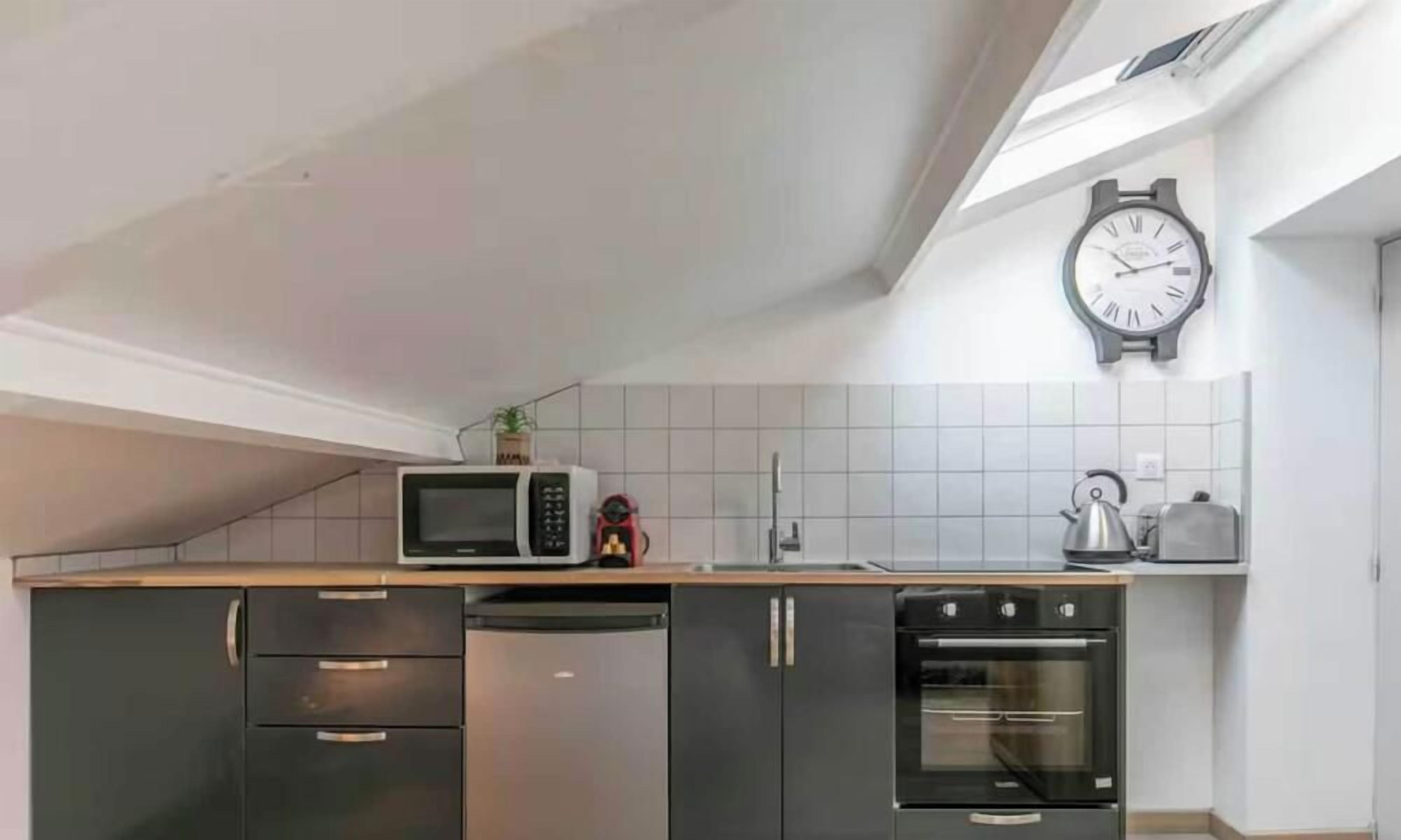 A kitchen with a microwave, kettle, toaster, and a clock on the wall.