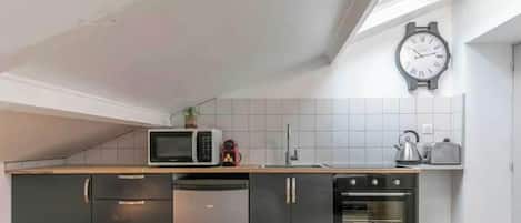 A kitchen with a microwave, kettle, toaster, and a clock on the wall.