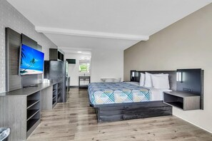 Ett modernt hotellrum med en säng, en TV, ett skrivbord och ett litet kök.