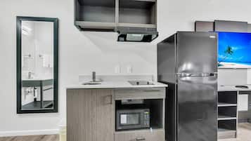 Cozinha moderna com micro-ondas embutido, geladeira de aço inoxidável e televisão exibindo uma paisagem de praia tropical.