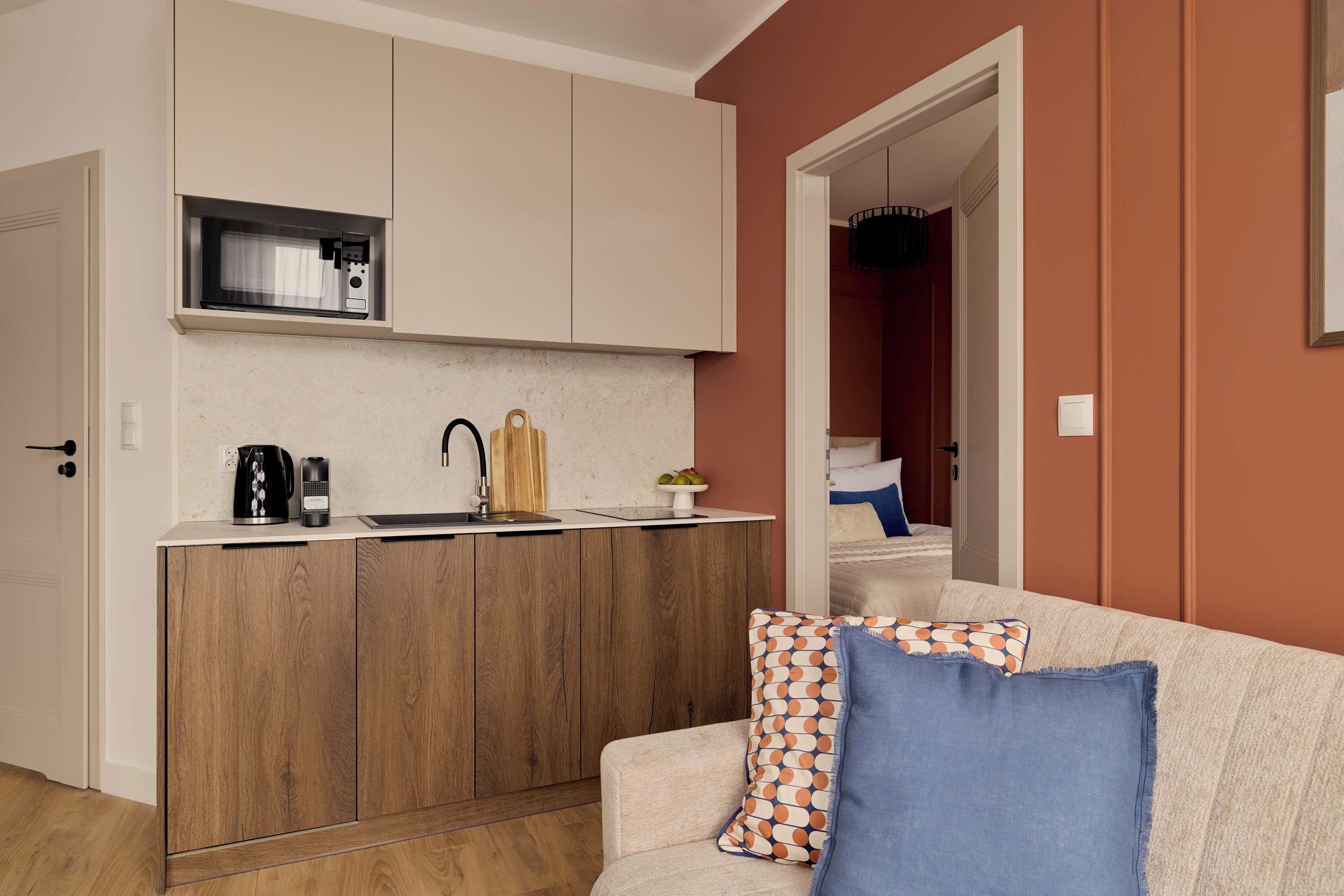 Un espacio habitable pequeño con kitchenette, un sofá con cojines estampados y una puerta visible que conduce a otra habitación.