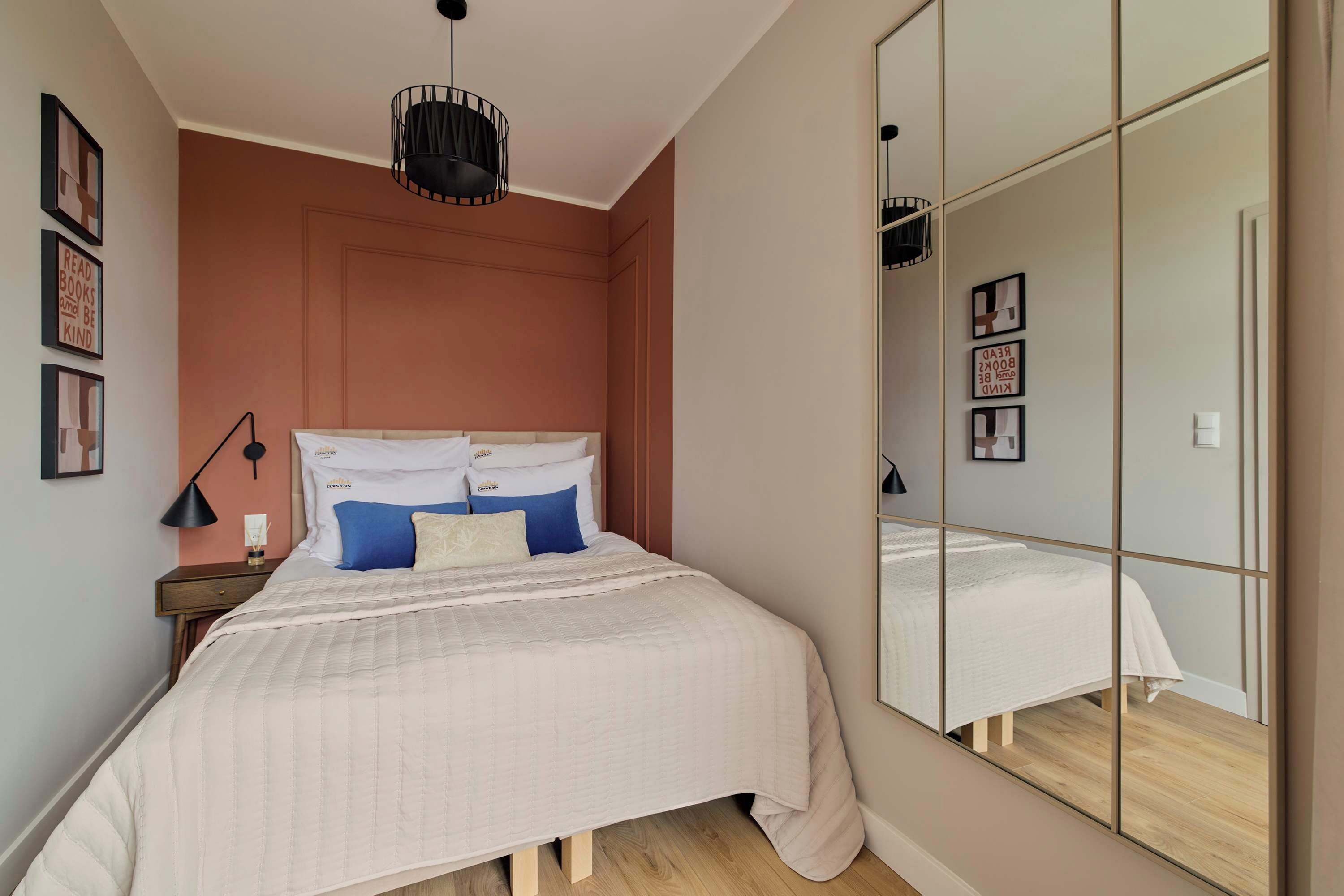 A bedroom with a bed, bedside tables, a mirror, and wall-mounted artwork.