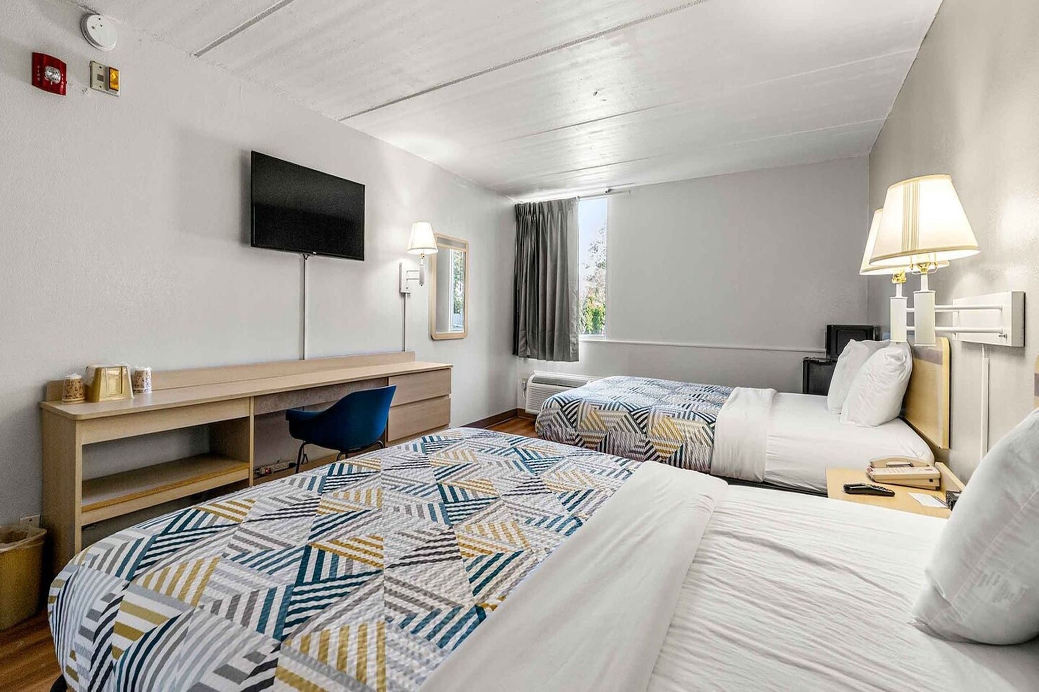 Habitación de hotel con dos camas, un escritorio, una silla, un televisor y una ventana con cortinas.