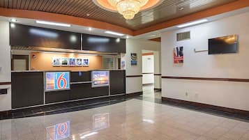 Un vestíbulo de hotel con una mesa de recepción, pantallas digitales, una araña y un piso de baldosas.