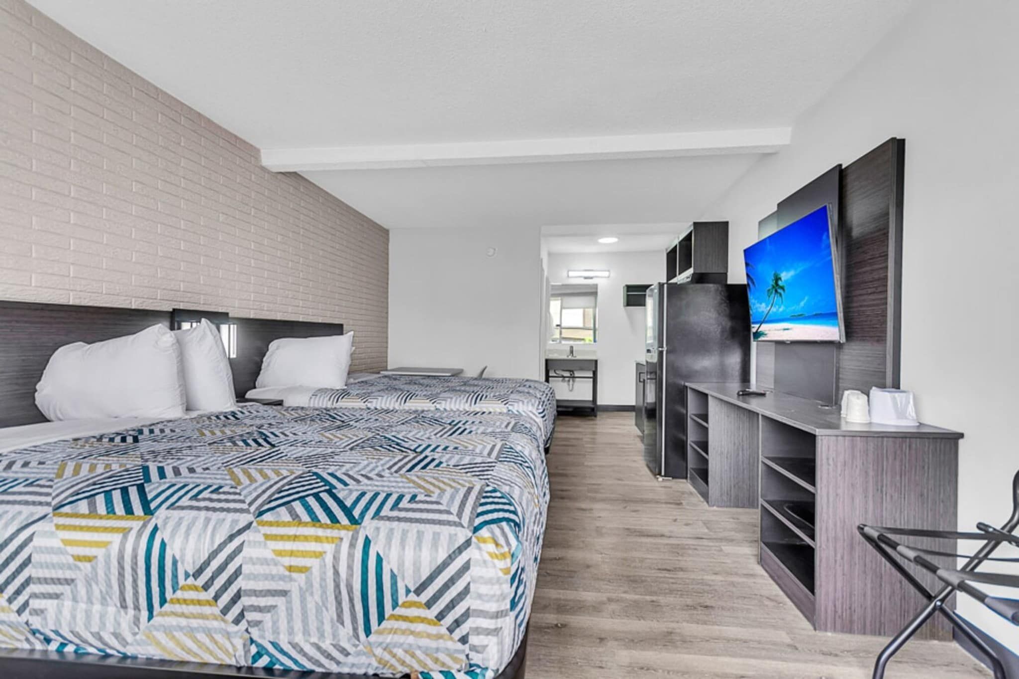 Une chambre d’hôtel avec un grand lit, une télévision, une kitchenette et un mur en briques.