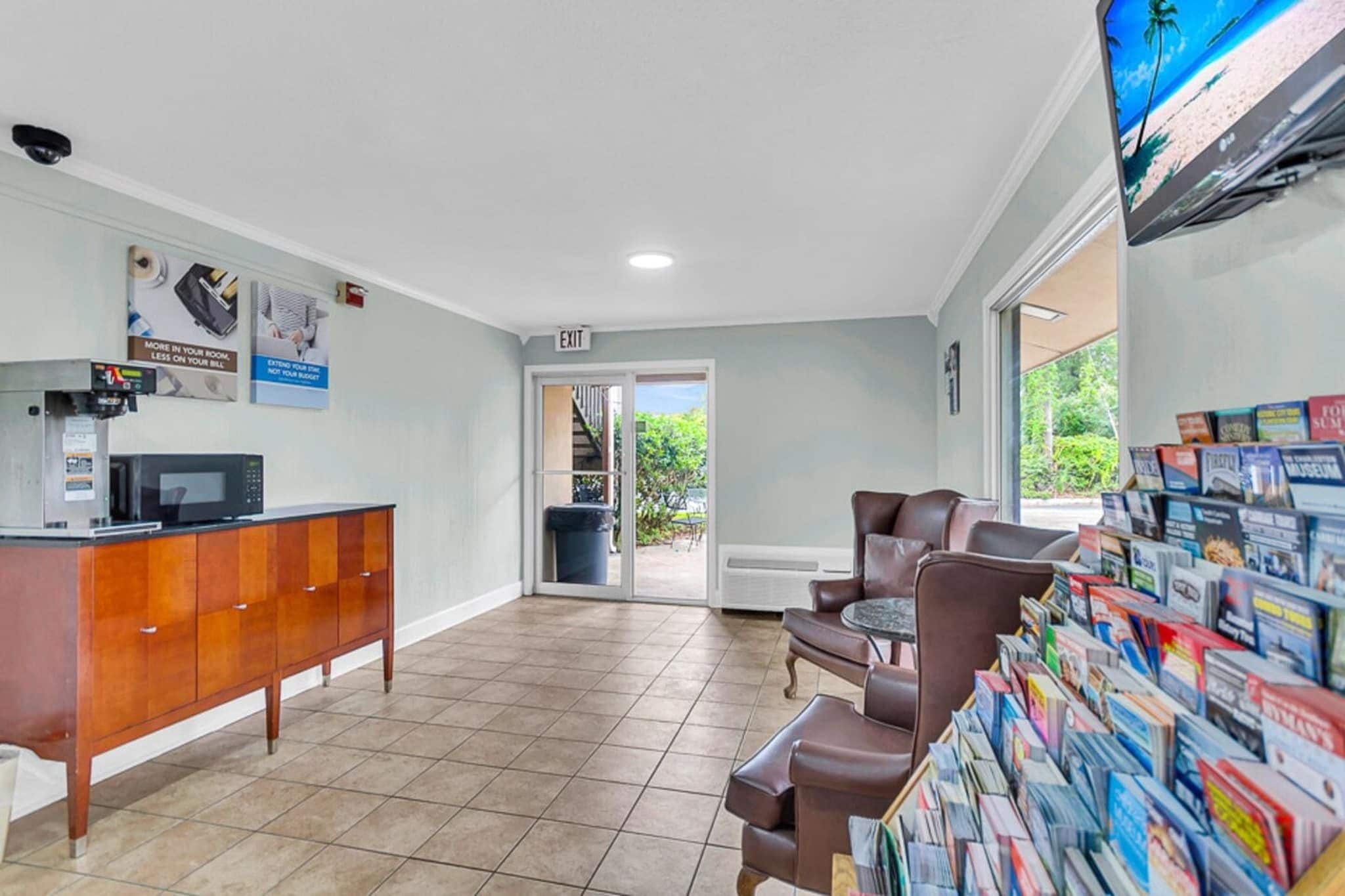 A reception area with a counter, a seating area with chairs, a wall-mounted display of magazines, and an exit sign.