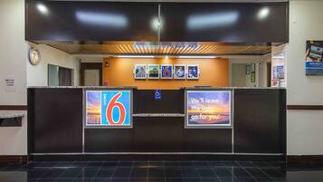 A hotel reception area with a digital display board, a wheelchair accessibility sign, and a clock.