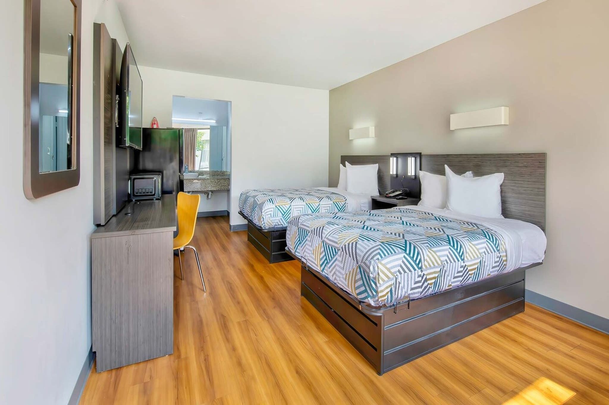 A hotel room with a bed, bedside tables, a desk, a chair, and a kitchenette.