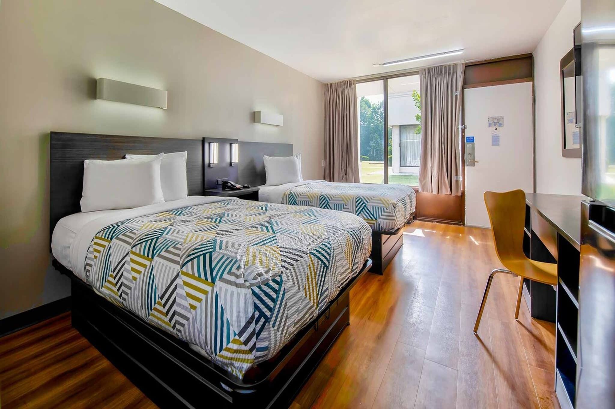 A hotel room with two beds, a desk, a chair, and a television.