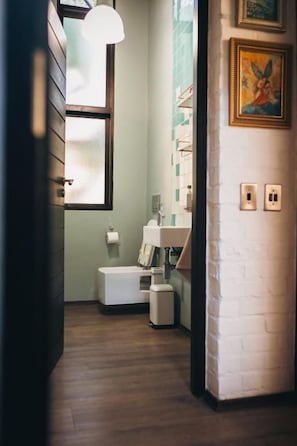 A narrow hallway with a wooden floor, a white bench, a small trash bin, and a wall-mounted light fixture. - studio21 seven (Pretoria)